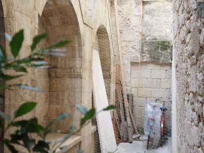 Attraverso un accesso laterale entriamo poi in uno stretto corridoio scoperto ricavato tra la chiesa e il fabbricato accanto. Fra travi in legno accatastate, biciclette rotte e altre cianfrusaglie...
